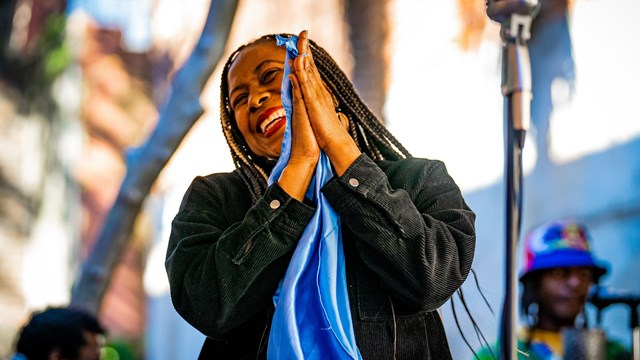 a black woman with braids holding a blue cloth while smiling.