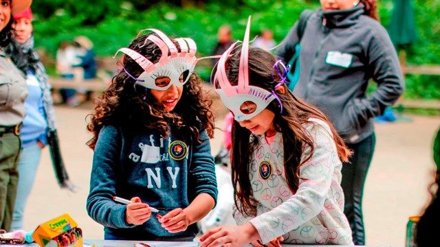 Two children make and wear colorful bird masks