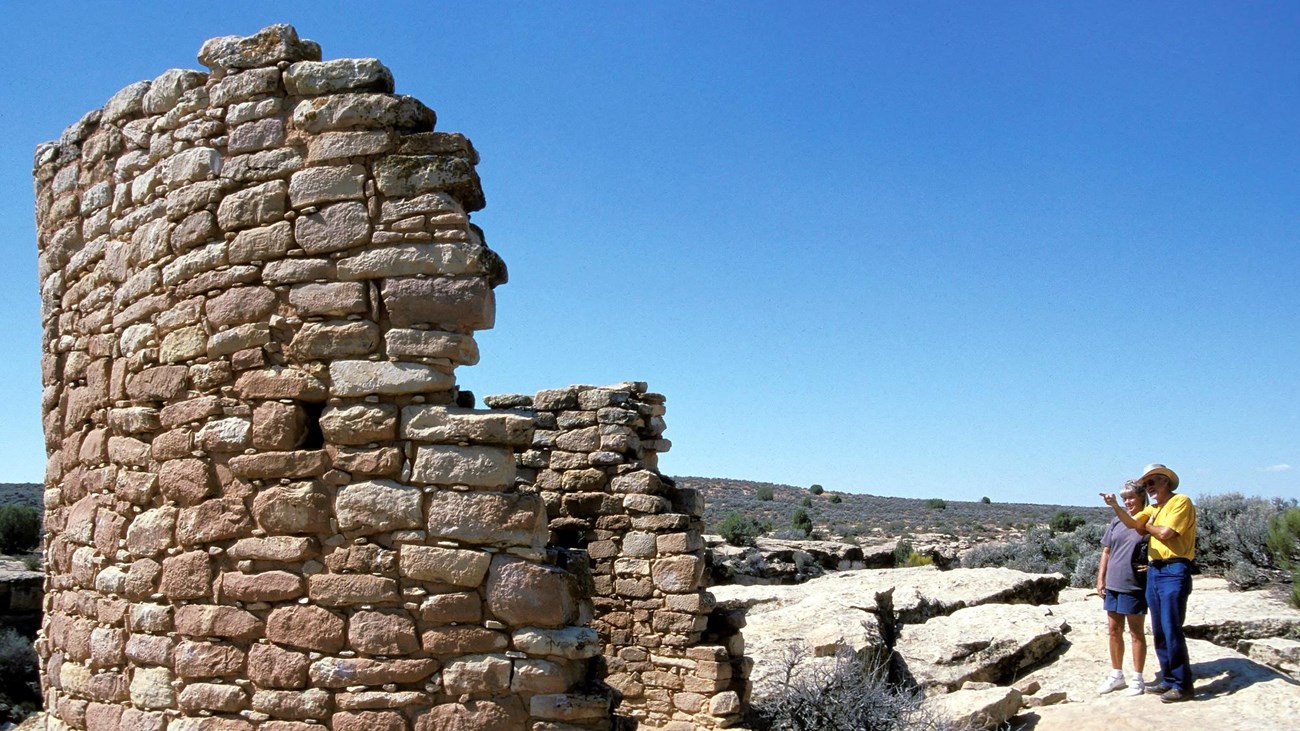 two people stare at a circular tower constructed of stones, part of it is missing.