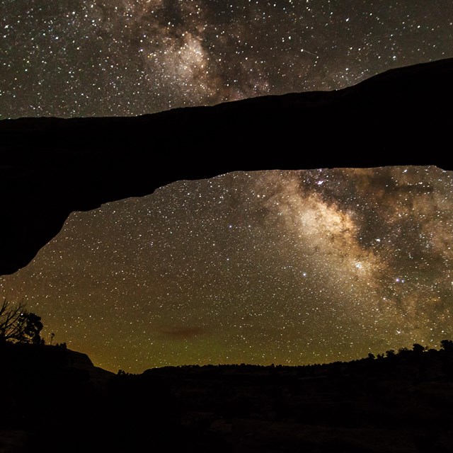 a massive stone arch with the Milky Way and stars overhead