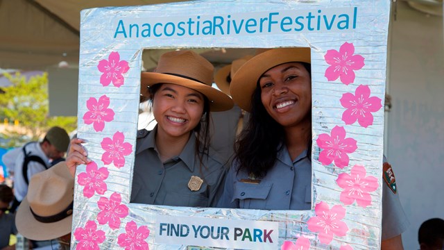 Two rangers pose in a frame with flowers on it.