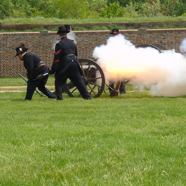 An artillery crew in historical clothing fires a field cannon