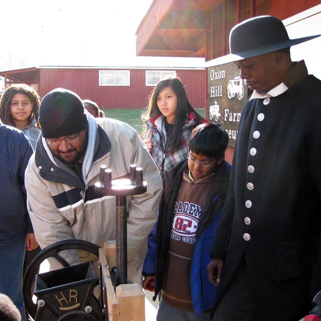 A man dressed in historical clothing teaches a group of people how to make cider