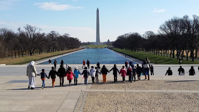Line of kids holding hands facing the reflecting pool.