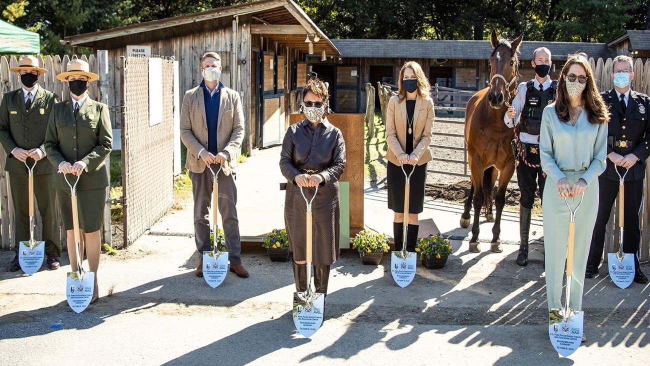 Women and men pose with ceremonial shovels at a stable.