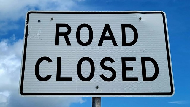White sign with black lettering that says "Road Closed"