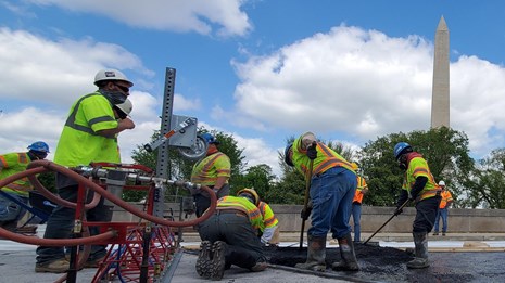 Construction workers operate testing equipment on road overpass bridge.