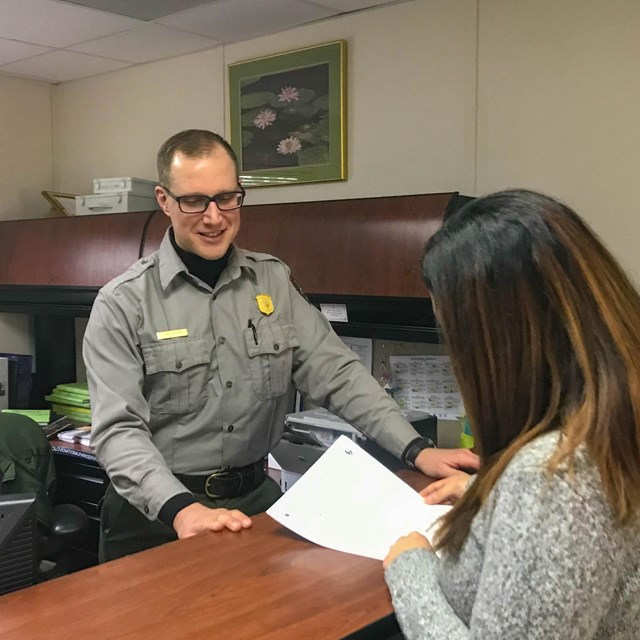 Ranger behind a desk talking to someone submitting paperwork