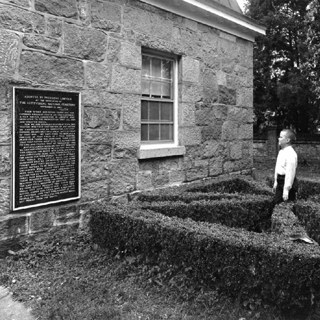 1968 photo of young boy in center of cross hedge, looking at Gettysburg Address tablet on lodge wall