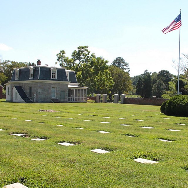 Grave markers are placed in neat lines in short turf, with a lodge, wall, and flagpole in background