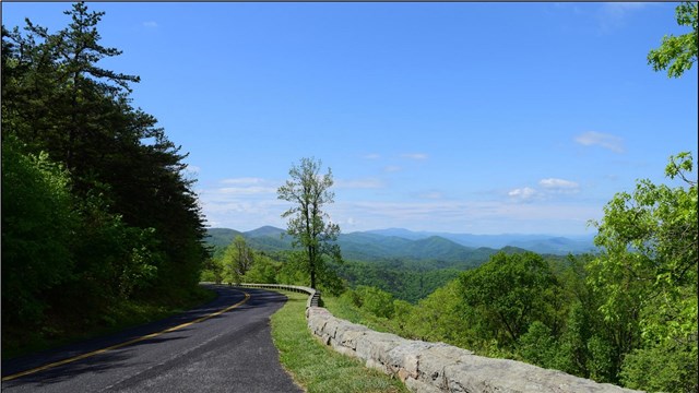 An asphalt road winding along a ridge with mountains in the distance. 