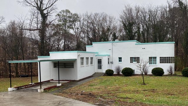 An L-shaped house with curved walls, glass block windows, and a carport.