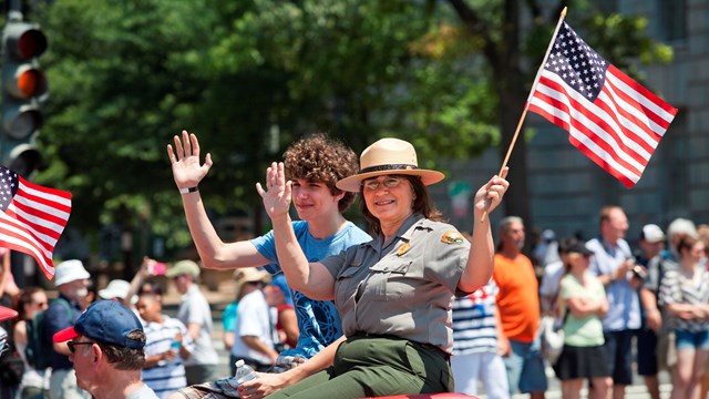A Park Ranger waves an American Flag from a parade car in the Independence Day Parade.