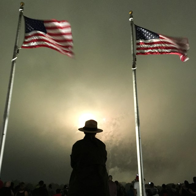 Ranger silhouette between flagpoles at night