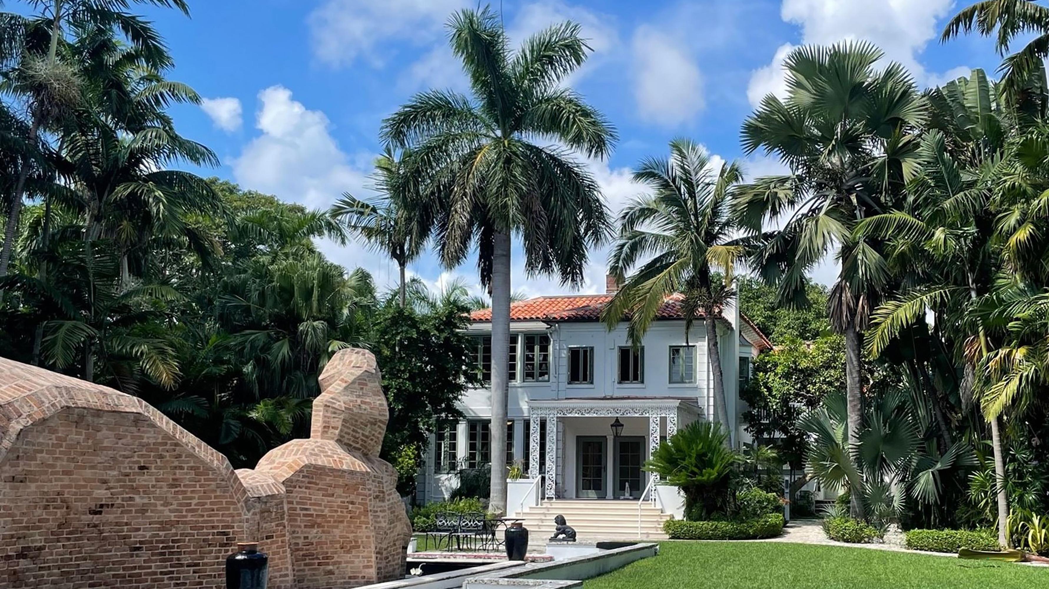 A white house with red tile roof surrounded by palm trees and a lawn