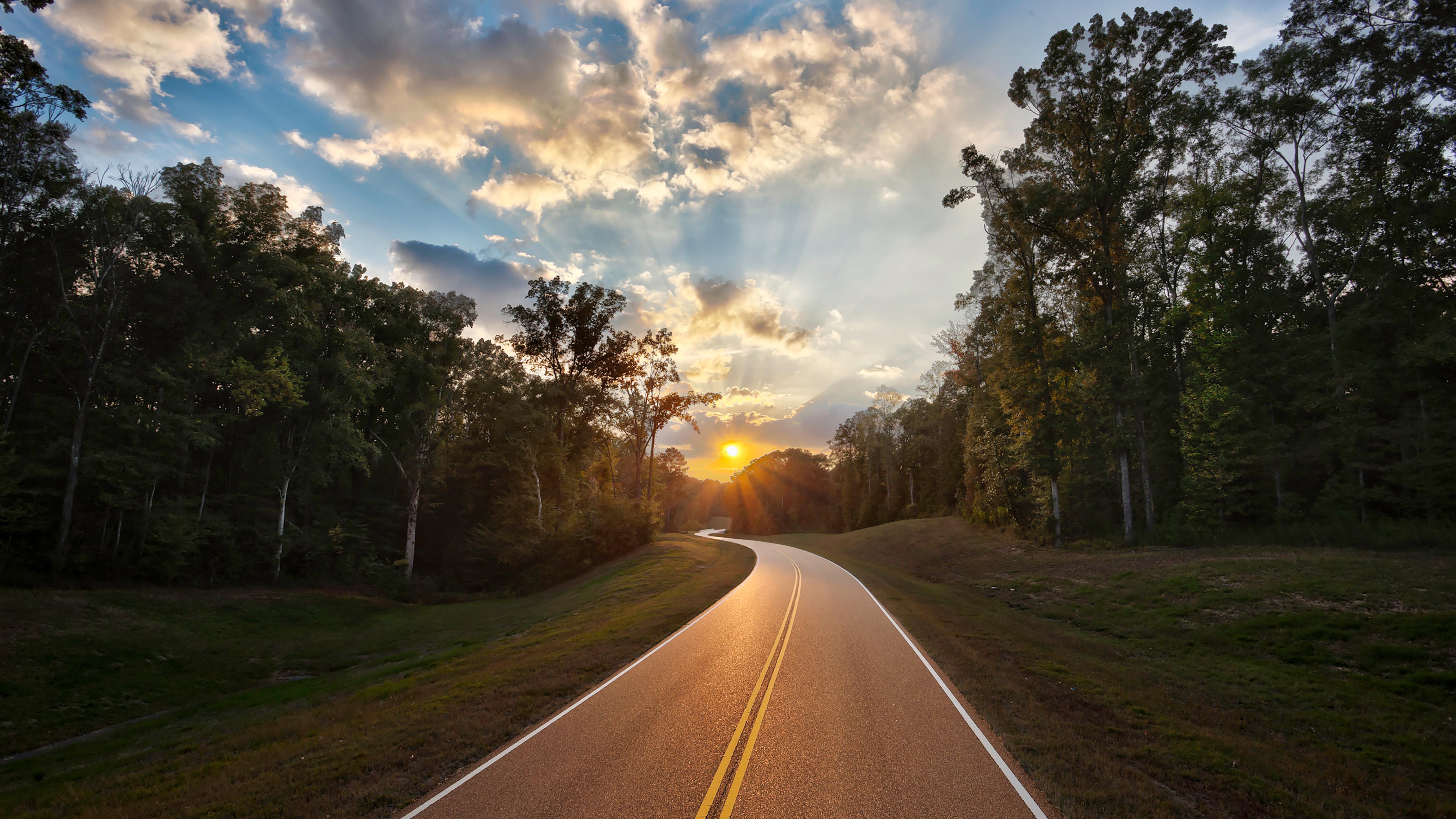 A two lane road heading into the sun rise.