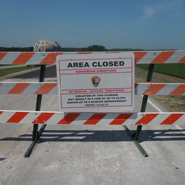 An orange and white wooden barrier with a sign stating road closed. 