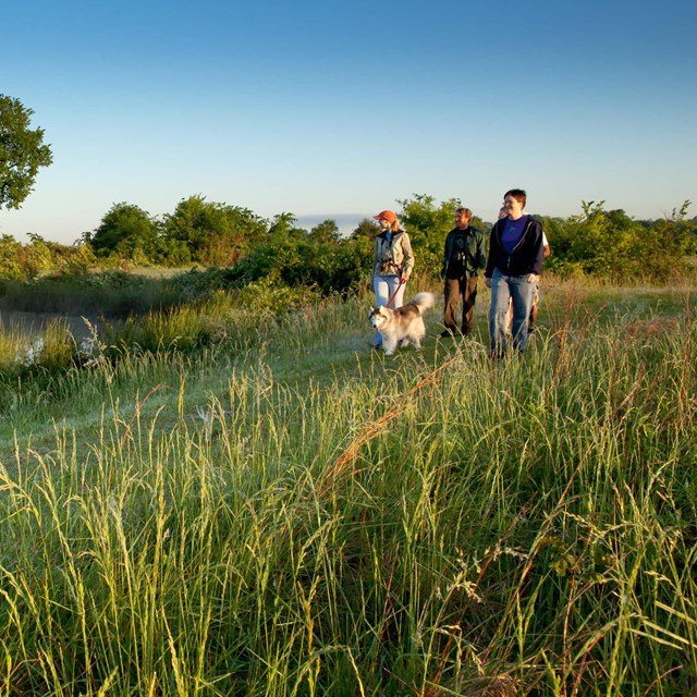 A group of hikers walk along a prairie trail.