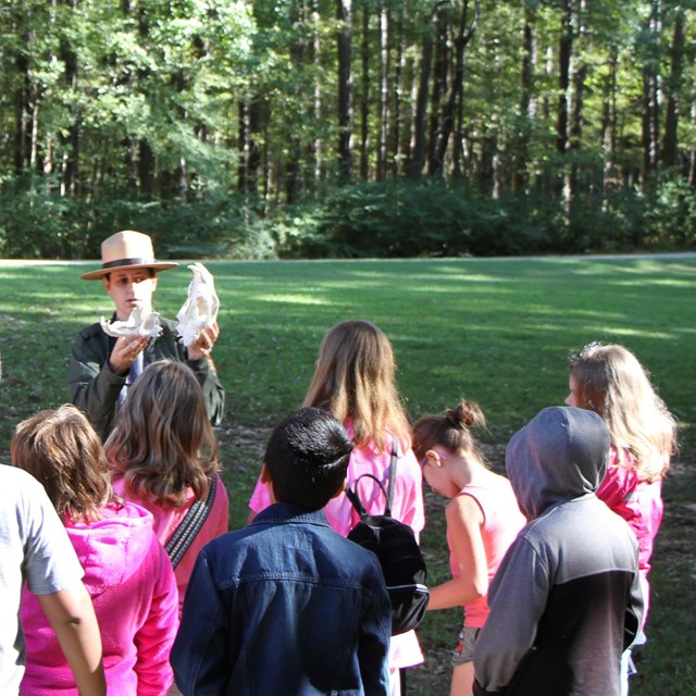 A park ranger presenting to young students outside.