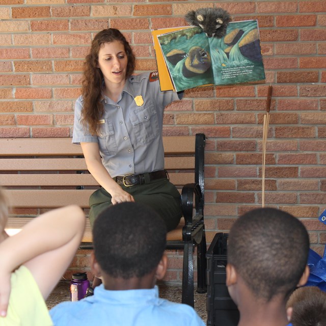 A park ranger holding up a book and reading to young children.