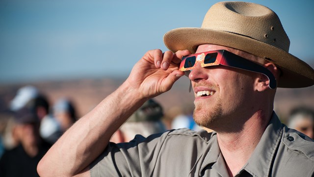 A ranger looks up at the sky through eclipse viewing glasses