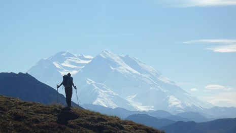 a backpacker stands on a mountaintop looking out to blue skies and mountains