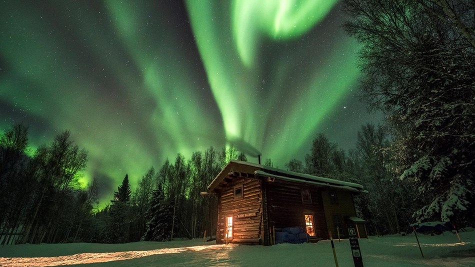 Northern lights over a cabin in the snowy woods Aurora dances and shimmers overhead above a cabin at