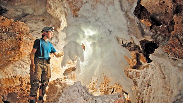 a caver stands next to a white crystal cave formation