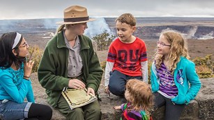 A ranger in a flat hat sits with children