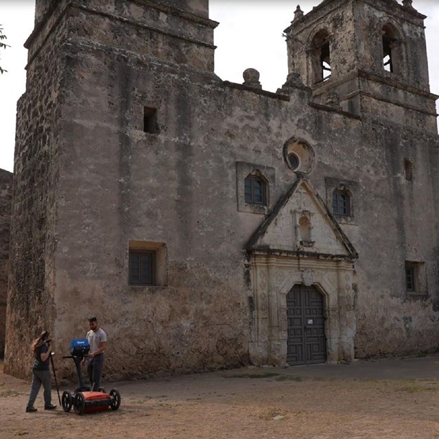 a historic stone mission with two scientists outside