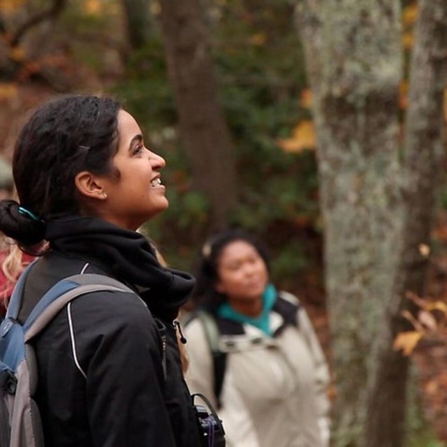 a woman of color smiles as she enjoys a fall forest with friends