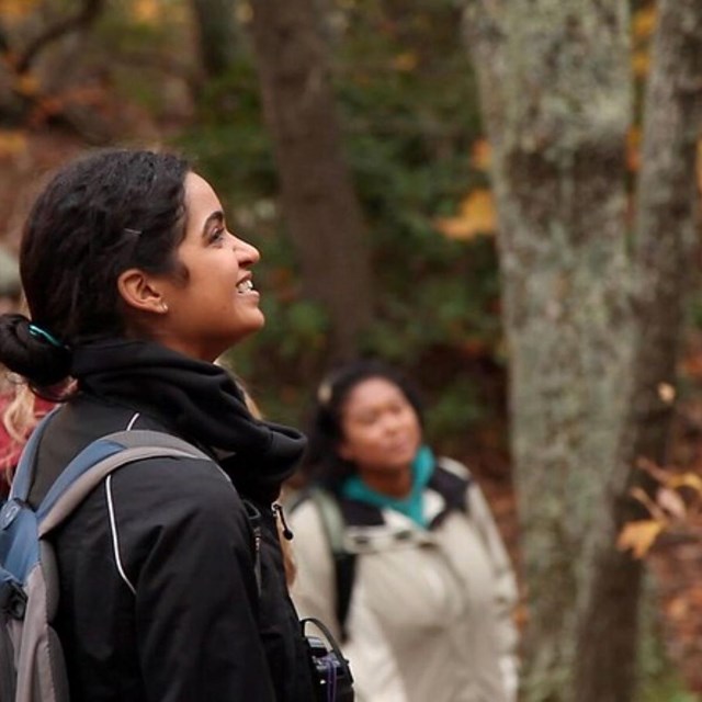 a woman of color smiles as she enjoys a fall forest with friends