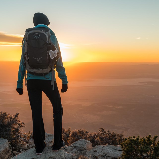 a hiker stands on a mountaintop enjoying the view at sunset