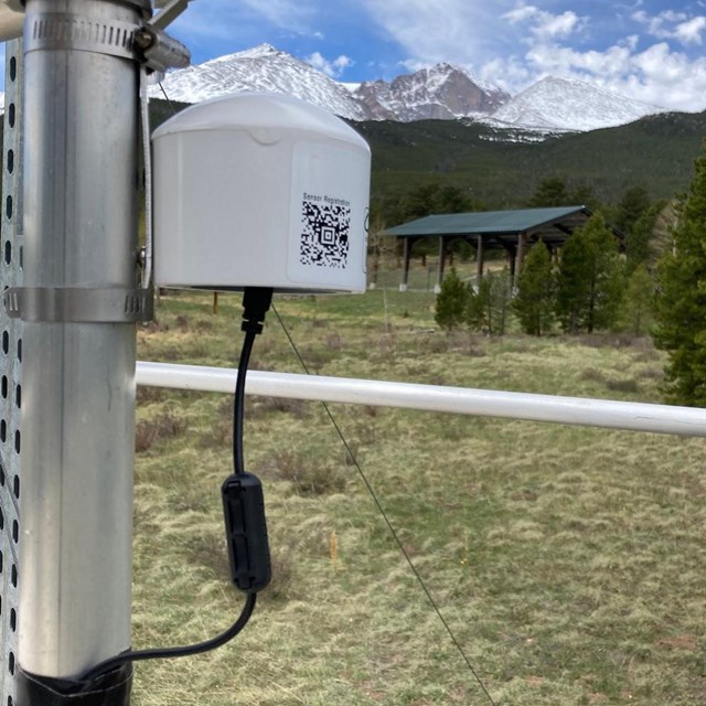 air quality monitoring equipment on a pole with trees and mountains in the background