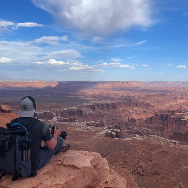 a person sits on a ledge overlooking canyons