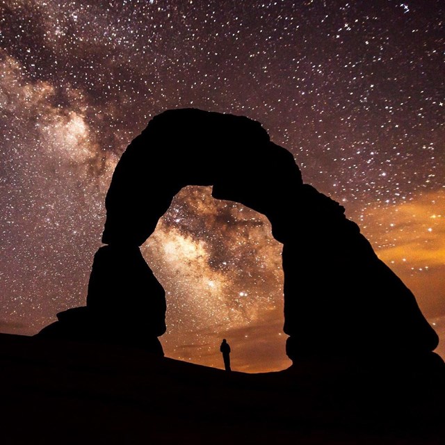 the milky way and a silhouetted person standing under a large arch