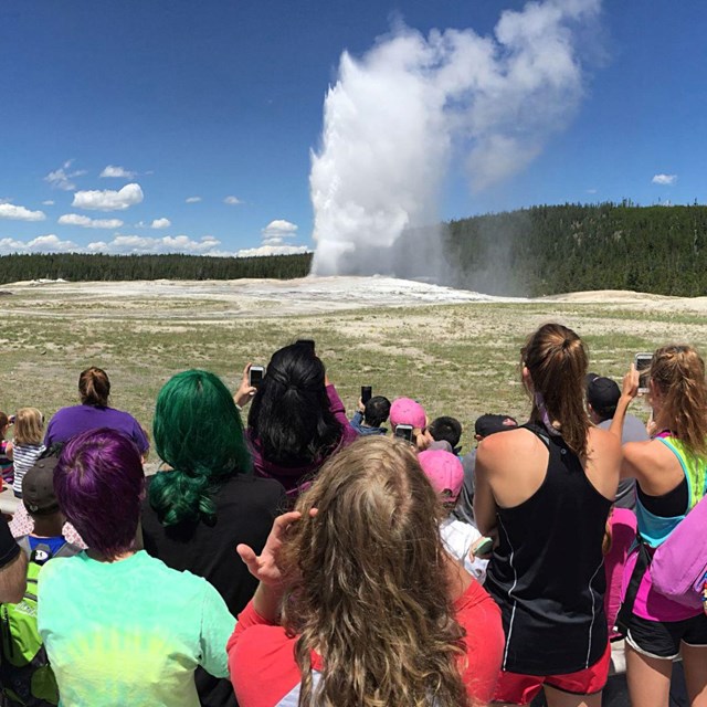 people gather to watch a geyser erupt
