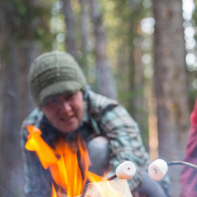 two smiling people roast marshmallows over a fire