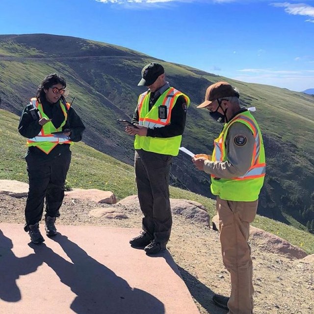 a group of volunteers wearing safety vests meet in a parking lot in an alpine area