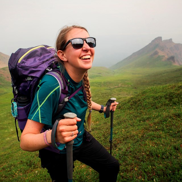 a smiling young woman with a backpack using hiking poles to hike outdoors