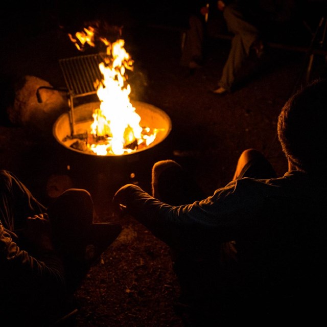 photo of 2 people sitting by a campfire