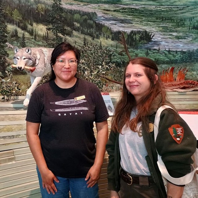 two women stand in front of a wolf display in a visitor center
