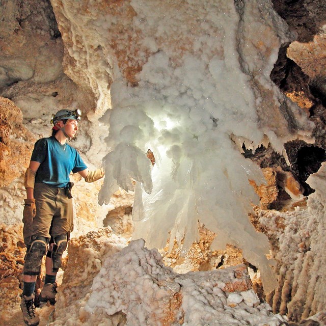 a caver stands next to a white crystal cave formation