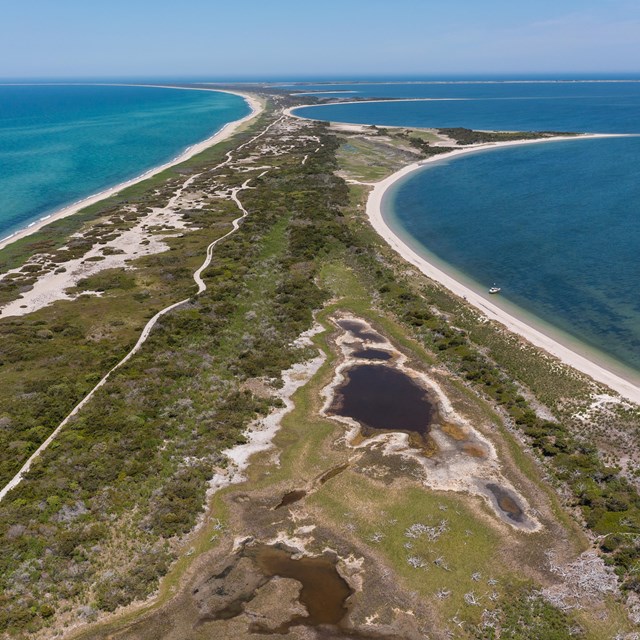 an aerial view of a thin spit of land with ocean on either side