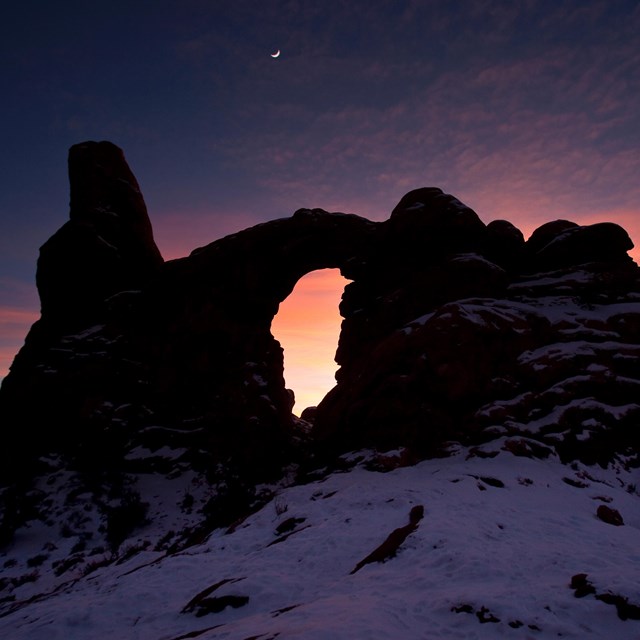 a rock arch formation silhouetted by a winter sunset