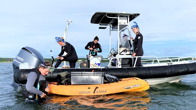 Five researchers on a motor boat in an estuary