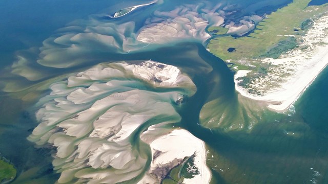An aerial view of a breached barrier island, with sand fanning outward in a series of swirls