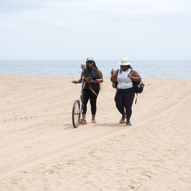 Two interns push a single-wheeled contraption across a beach