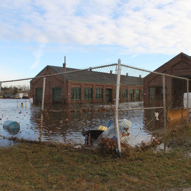 flood waters surround a brick building and chain link fence.