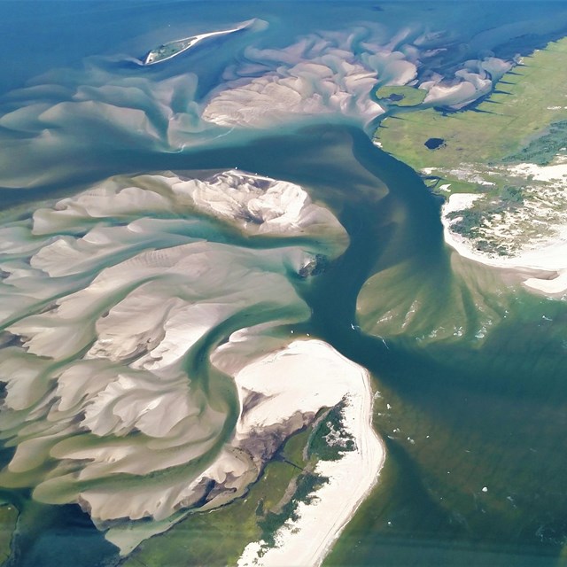 An aerial view of a breached barrier island, with sand fanning outward in a series of swirls